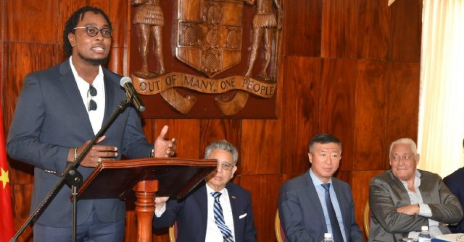Minister without Portfolio in the Office of the Prime Minister, Hon. Michael Henry (right), listens as Darrian Bryson speaks about his time spent in China, at a welcome reception at Jamaica House