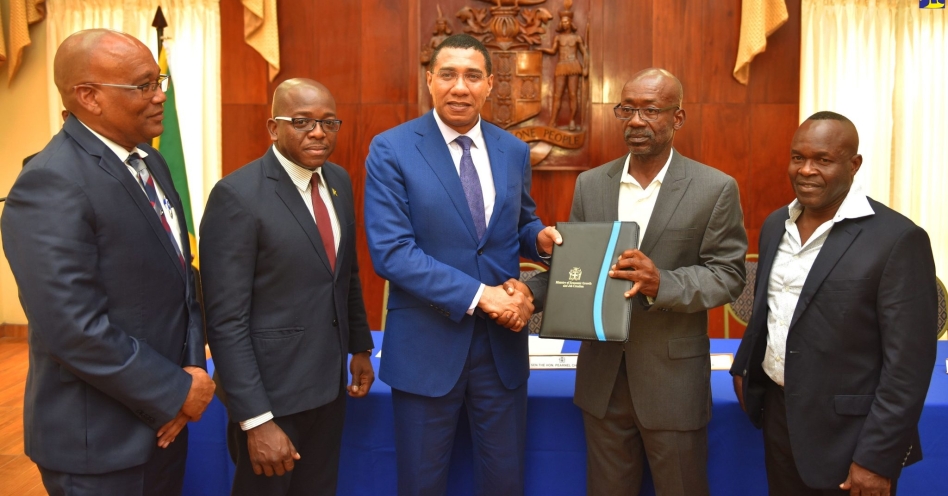 Prime Minister, the Most Hon. Andrew Holness (centre), presents Director, Rite Solutions Development Company, Owen Campbell (2nd right), with a signed copy of the joint venture agreement for the provision of 623 new solutions under the Shooter's Hill Housing Development project in Portmore, St. Catherine. The agreement, between the Housing Agency of Jamaica (HAJ) and Rite Solutions, was signed at Jamaica House on Thursday (Aug. 8). Others (from left) are: Chairman, HAJ, Norman Brown; Minister without Portfolio in the Ministry of Economic Growth and Job Creation, Senator the Hon. Pearnel Charles Jr.; and Director, Rite Solutions Development Company, Vincent Taylor.